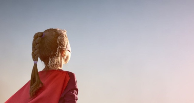 An animated child with hair tied back in a plait wearing a red cape and their back to the viewer as they look into the sun