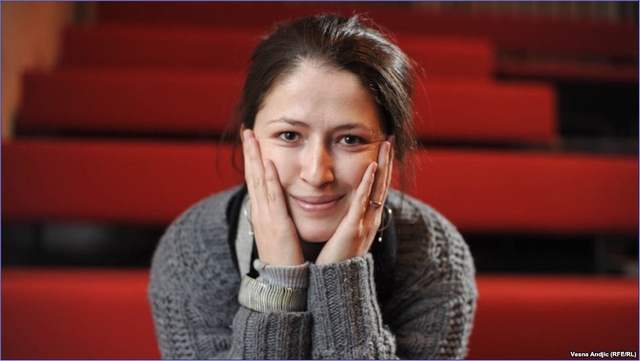 Head and shoulders picture of a woman sitting in a row of benches smiling at the camera