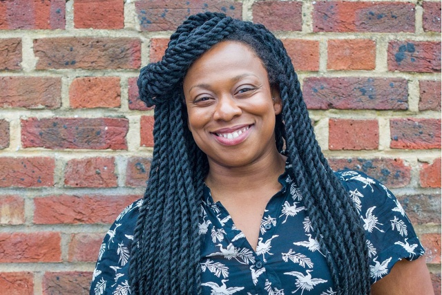 Vicki Amedume standing smiling in front of a red brick wall