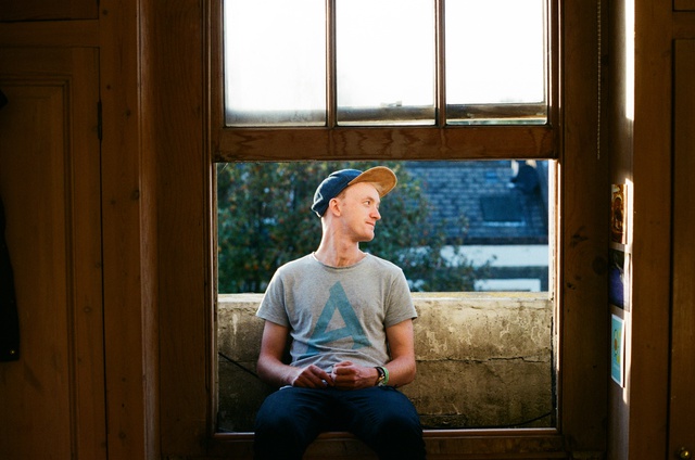 A man in a grey tshirt and cap sits outside an open wooden window