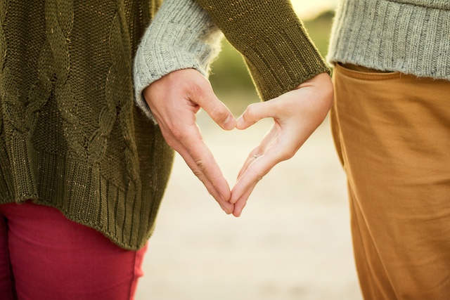 A photo of two people's hands linked together to form a heart shape