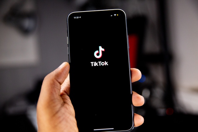 A white hand holds a phone with the pink and blue TikTok logo on it