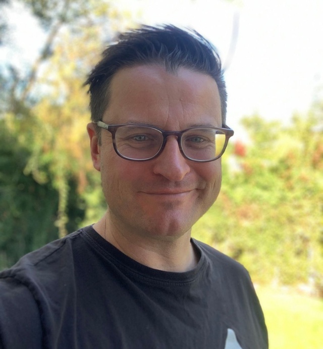 Headshot of Dan Pursey, a white man with dark hair wearing glasses and a black t-shirt