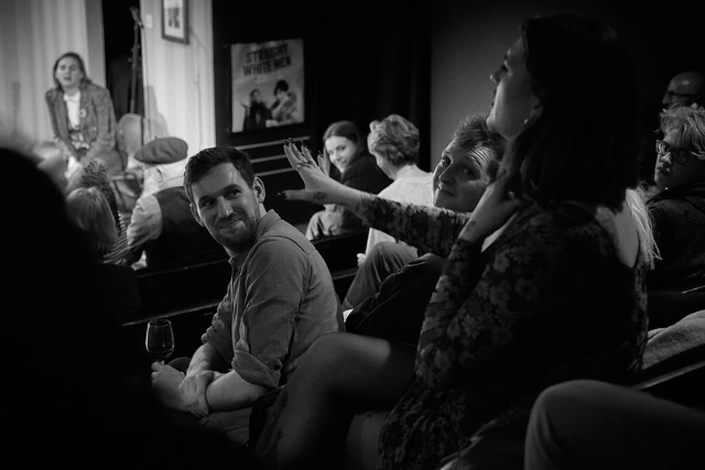 Black and white photo of a man in theatre seating watching a show and smiling