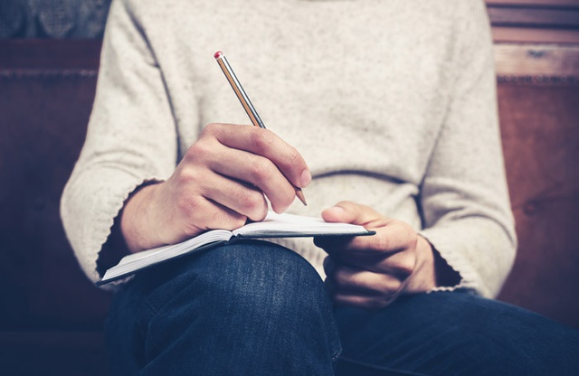 Close up of a hand writing in a notebook balanced on a knee