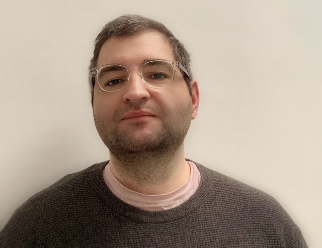 Headshot of a man with grey hair, transparent glasses and a brown jumper